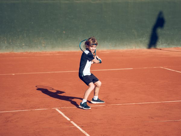 Athletic kid with racket playing tennis on clay court