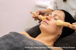 Crop beautician massage with brushes on female's cheeks in beauty salon 5lVZlY