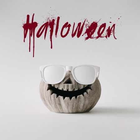 Pumpkin skull with sunglasses on light wall with “Halloween” text