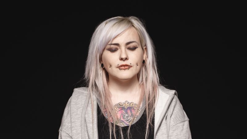 Woman with white hair and tattoo on body with her eyes closed