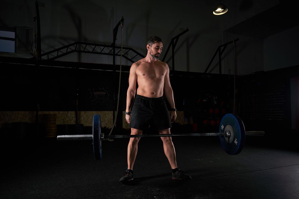 Muscular strong man preparing for lifting barbell with weights