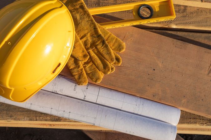 Abstract of Constrcution Hard Hat, Gloves, Level and House Plans Resting on Wood Planks