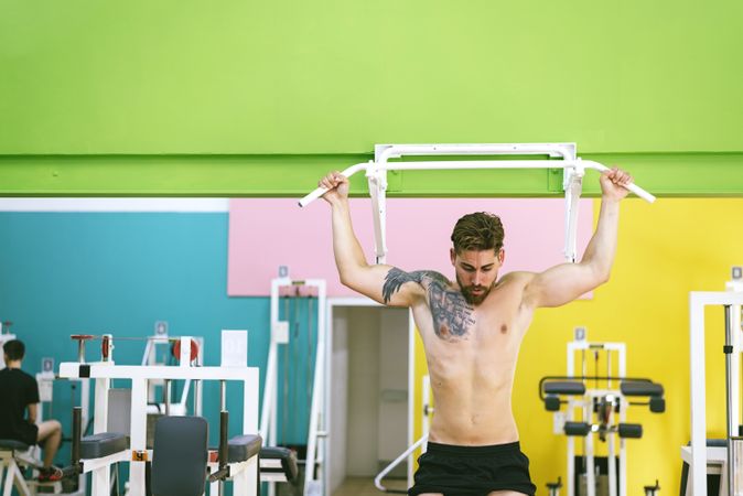 Front of man working out upper body in a fitness club on pull up bar, copy space