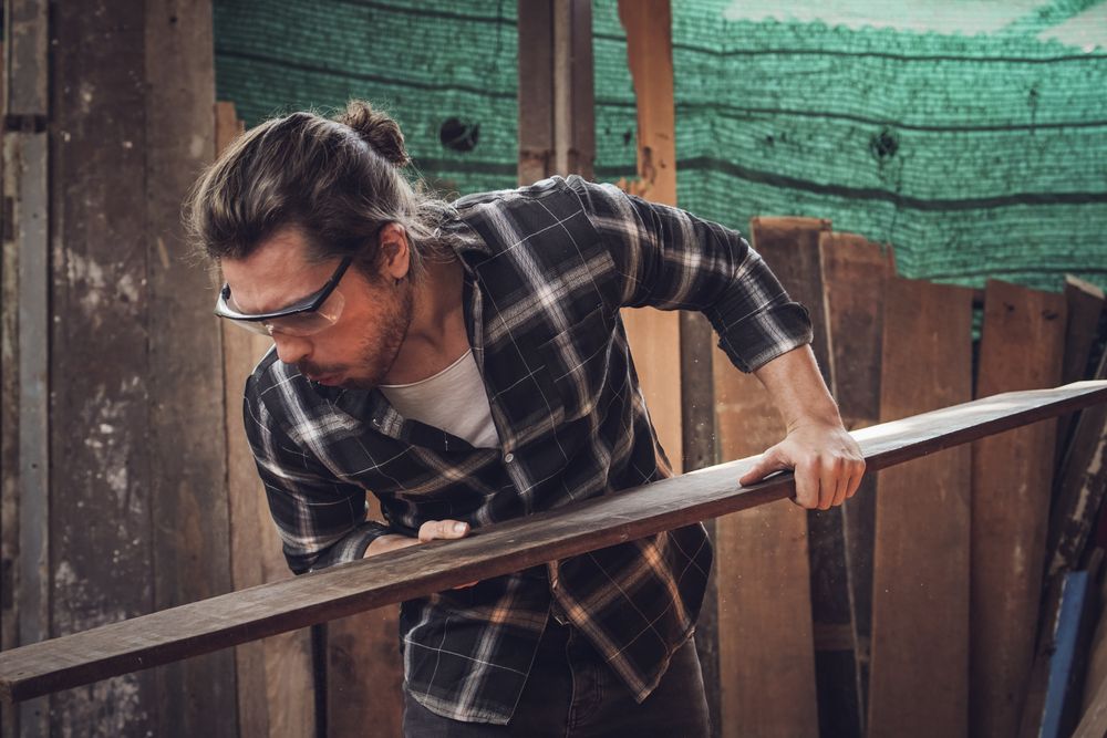 Male carpenter blowing dust on the wood board and checking quality