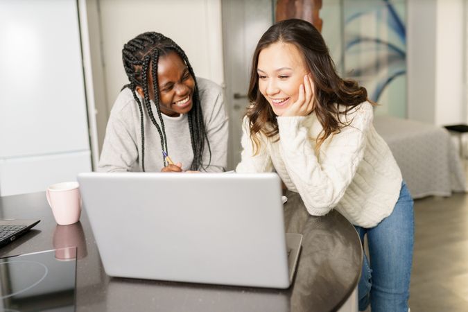 Two women sitting at kitchen table laughing at something on a pc