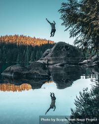 Person jumping on rock with reflection in lake water bYrxg0