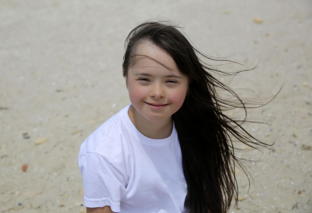 Happy girl with long dark hair on the beach smiling and looking at camera