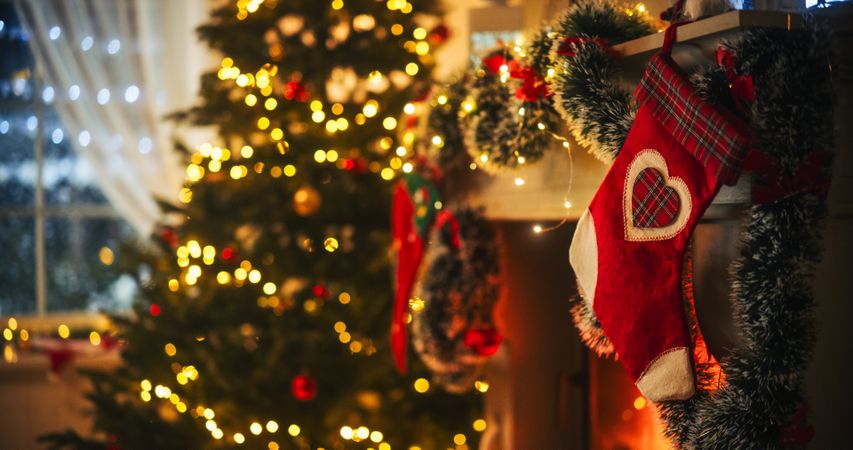 Empty Shot Depicting the Magic of Holidays on a Peaceful Snowy Christmas Eve: Close Up on Decorated Fireplace with Stockings Next to a Christmas Tree.