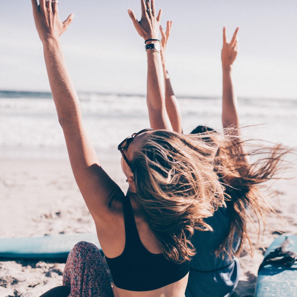 Two young women raising their hands in the air at the beach