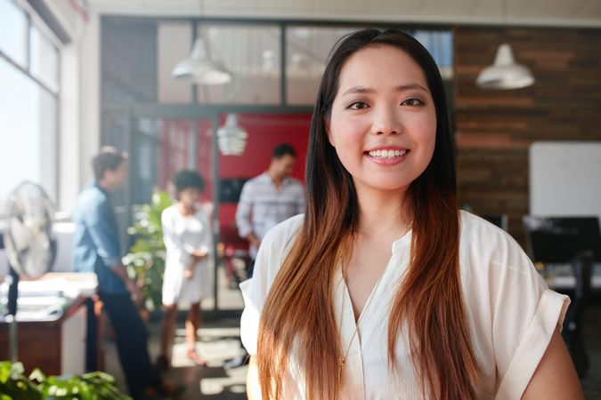 Smiling woman standing in office with employees in background