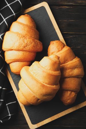 Vertical composition of bread board with croissants on table with kitchen towel, top view