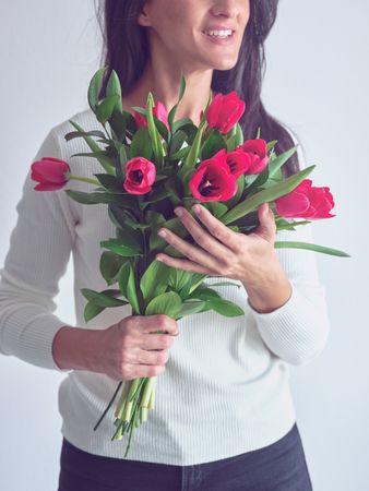 Crop happy woman with bouquet of fresh red tulips