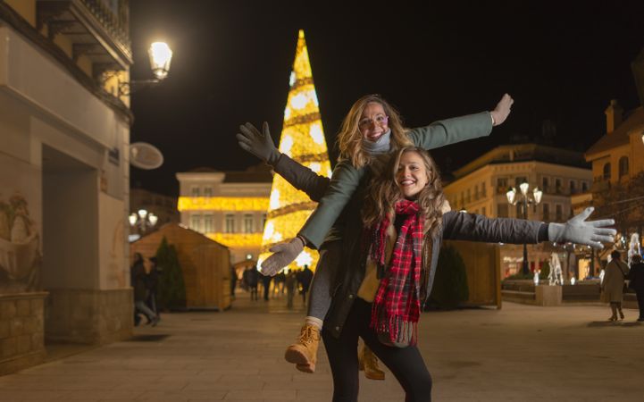 Happy women with piggyback ride and raised arms on street