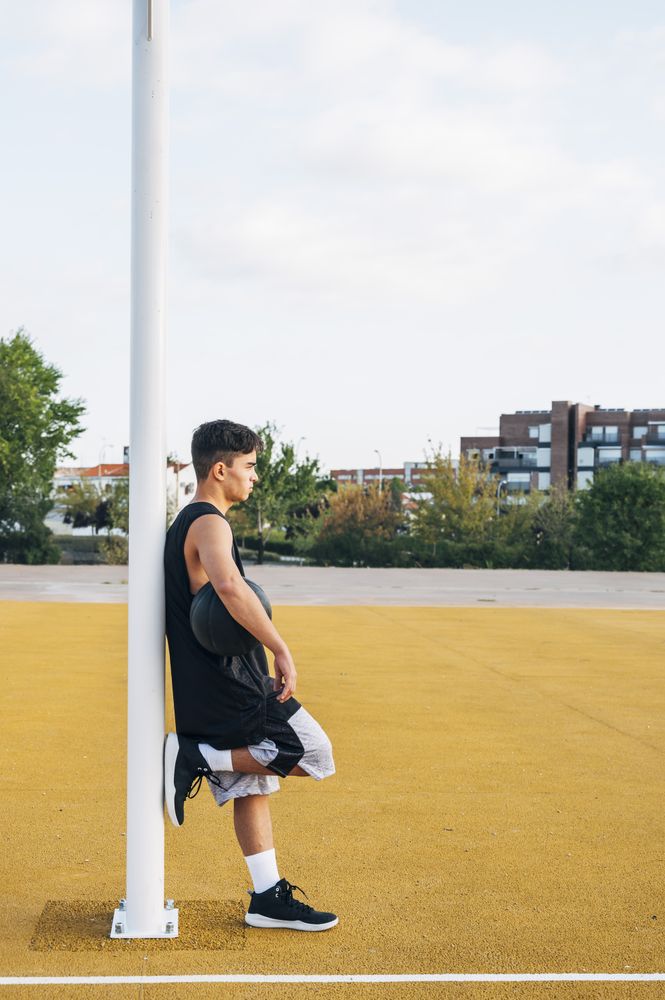 Young man leaning on basket on basketball court outdoor.