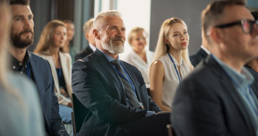 CEO Sitting In Crowd At International Technology Conference, Listening To Presentations From Startup Companies With Innovative Products or Services.