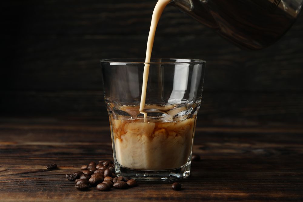 Milk is poured into a glass of coffee. Composition with ice coffee