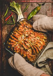 Grey oven mitts holding a roasted squash casserole against wooden surface, vertical composition