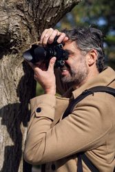 Smiling man leaning on tree and taking photo in woods