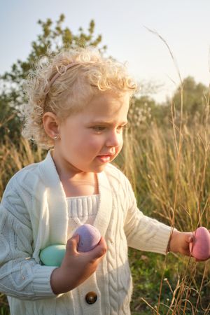 Cute little girl collecting Easter eggs in sunny countryside