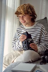 Cheerful boy with retro photo camera on bed