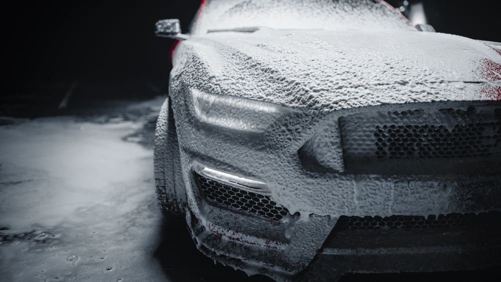 Modern Red Performance Vehicle Headlights Covered in Shampoo, Being Cleaned at a Dealership Car Wash.