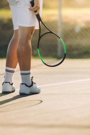 Cropped shot of sportsperson with racket on tennis court