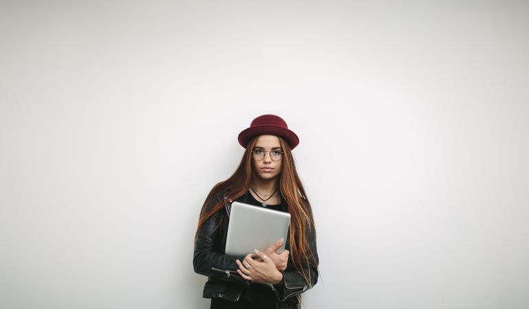Stylish woman holding laptop standing against a light wall