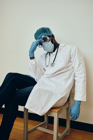 Tired Black male doctor in ppe gear sitting down in hospital