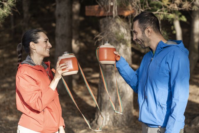 Couple toasting with vintage canteens during outdoor hike in forest
