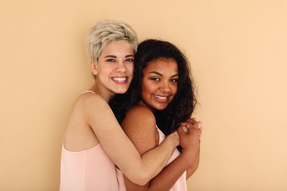White blonde woman hugging biracial friend in studio shoot