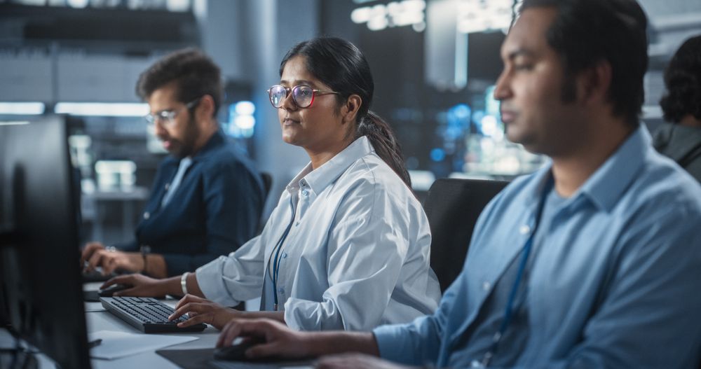 Young Team of Female and Male South Asian Specialists Working on Computers and Having a Conversation at a Workplace.