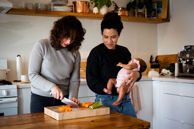 Happy female couple and baby in kitchen preparing food