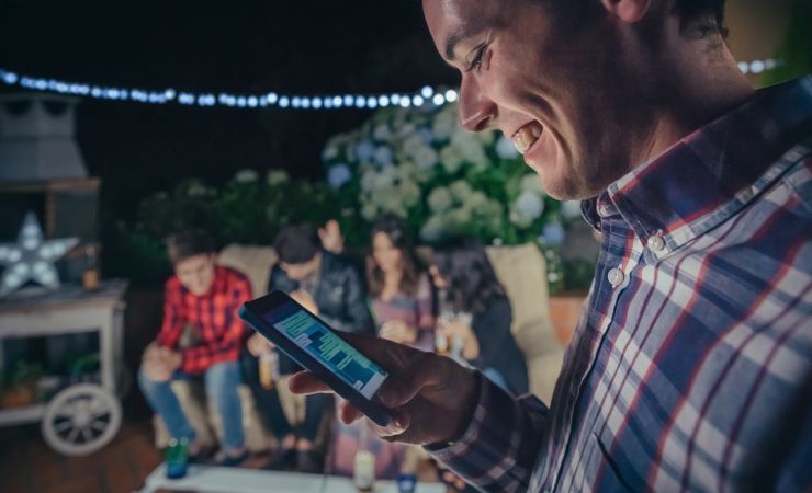 Smiling man looking smartphone at a party with friends