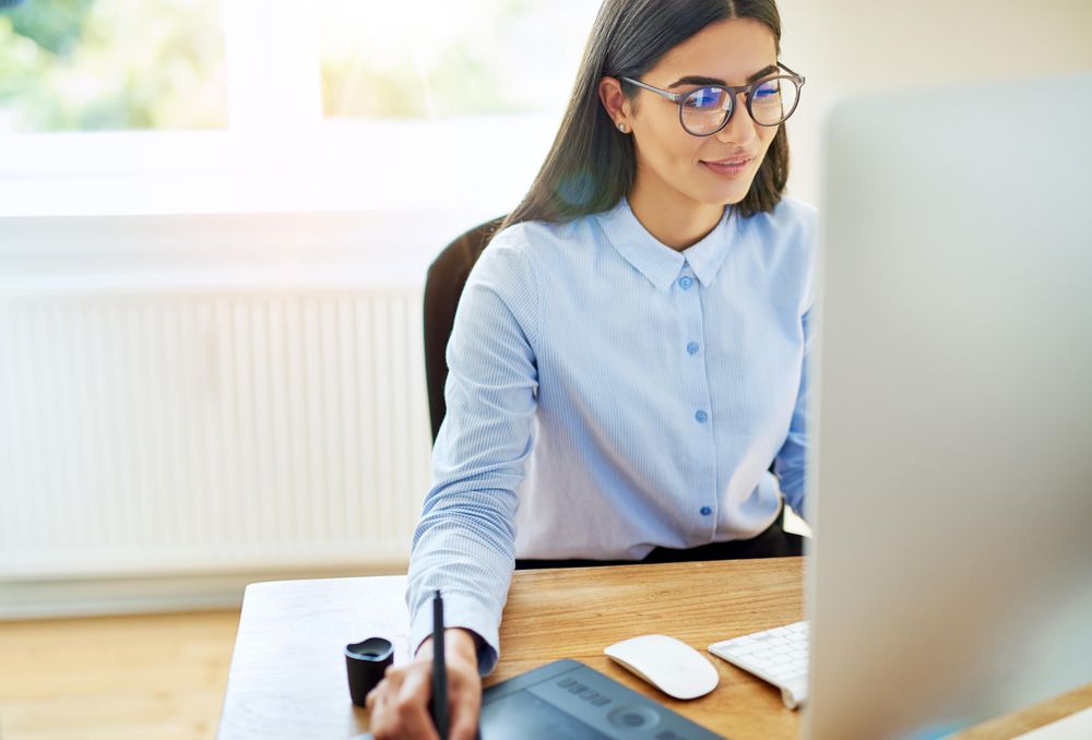 Arab woman working as a graphic designer from her desk using stylus and drawing pad