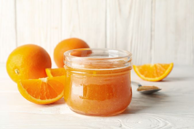 Oranges, spoon and glass jar with jam on wooden background