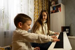 Boy presses piano keys while girl watches in surprise.