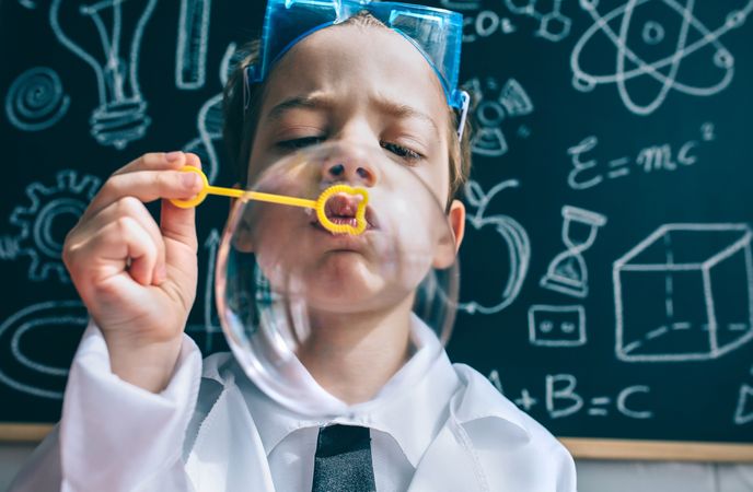 Kid blowing soap bubbles against of science doodles on board