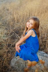 Female child sitting on bolder in field, vertical