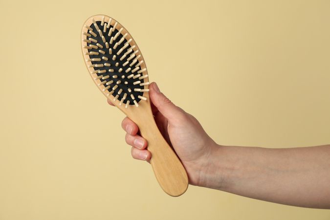 Female hand holds hair brush on beige background, close up