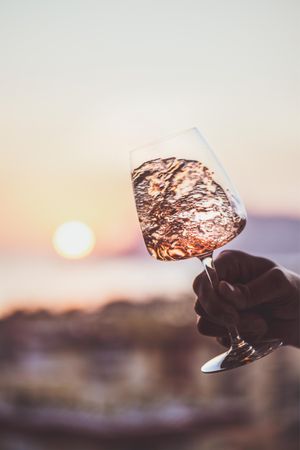 Man's hand swirling glass of rose wine against sunset, vertical composition