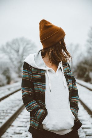 Woman wearing brown knit cap standing on snow covered train rail