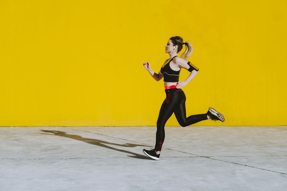 Woman with earphones running near wall