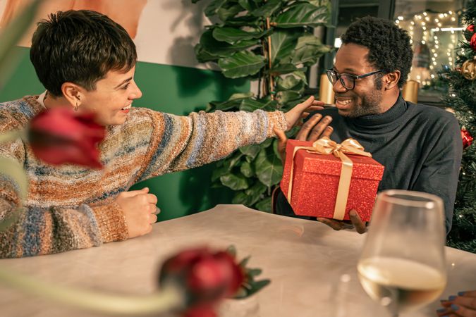 Happy diverse couple talking and sharing a gift during a Christmas celebration