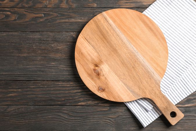 Cutting board with kitchen towel on wooden background, space for text
