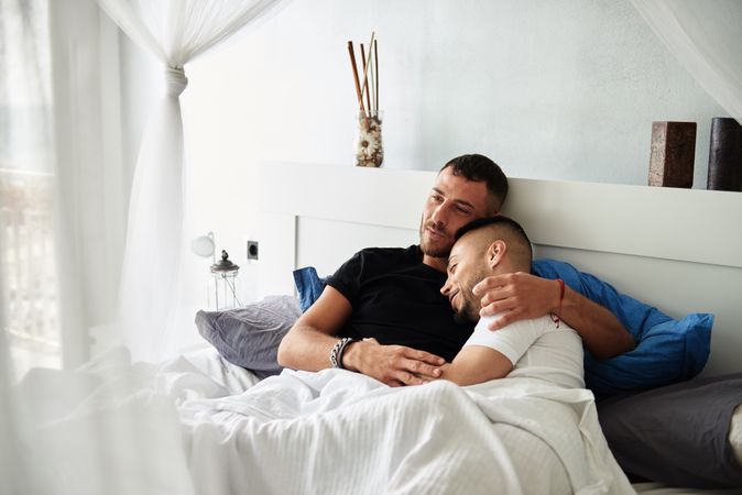 Smiling gay couple hugging on bed