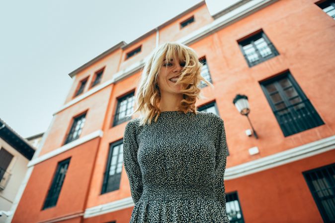 Looking up at smiling blonde woman standing by red building