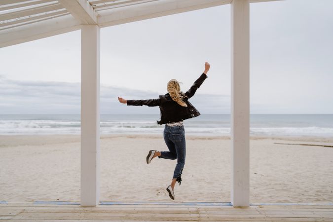 Joyful woman jumping raising hands up on wooden beach pier
