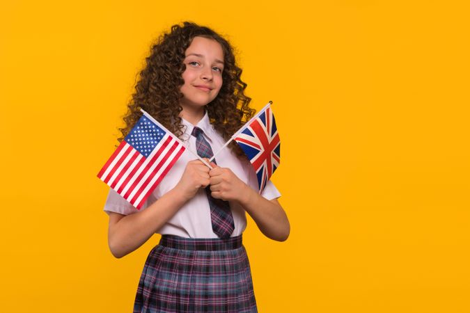 Girl with slight smile holding USA and UK flags.
