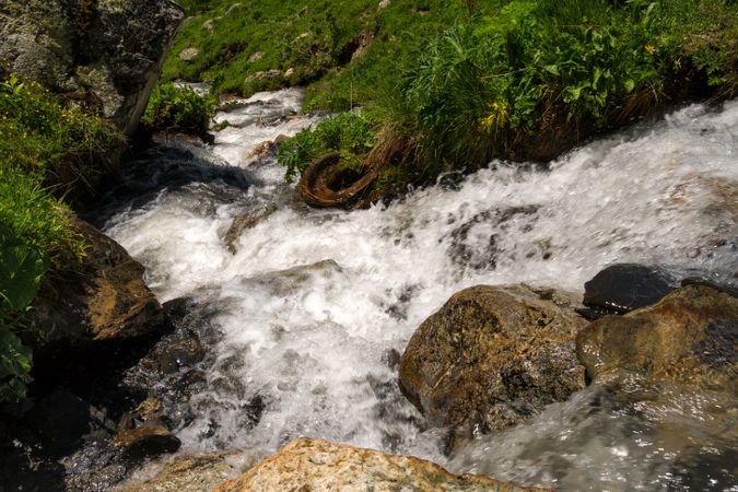 Turbulent mountain stream with rocky surroundings and green vegetation.