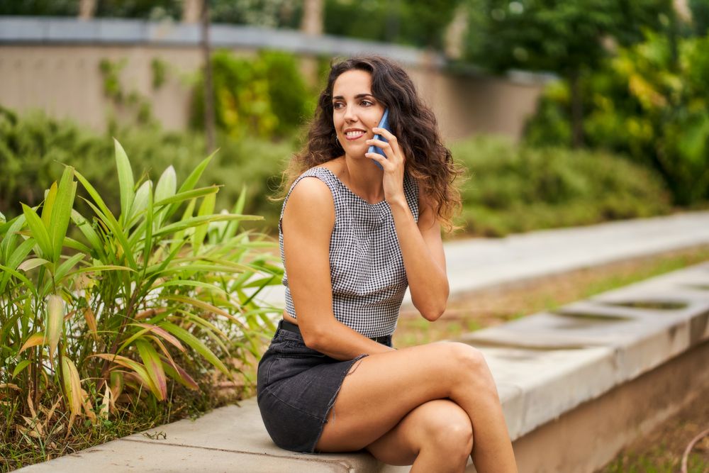happy young woman talking on mobile phone sitting in park